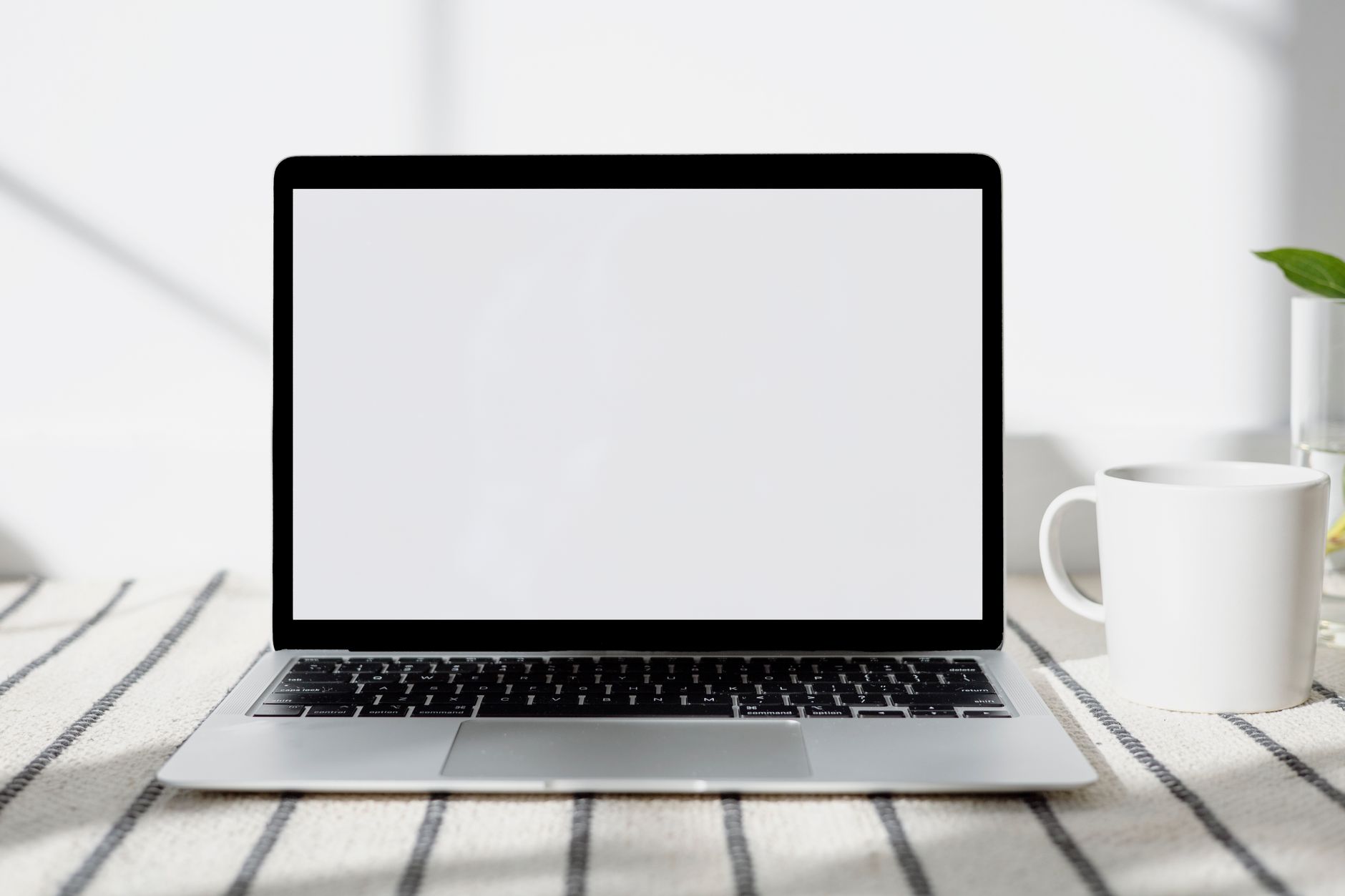 Minimalistisk hjemmekontor med en bærbar computer med tom skærm og en kop kaffe i naturligt lys