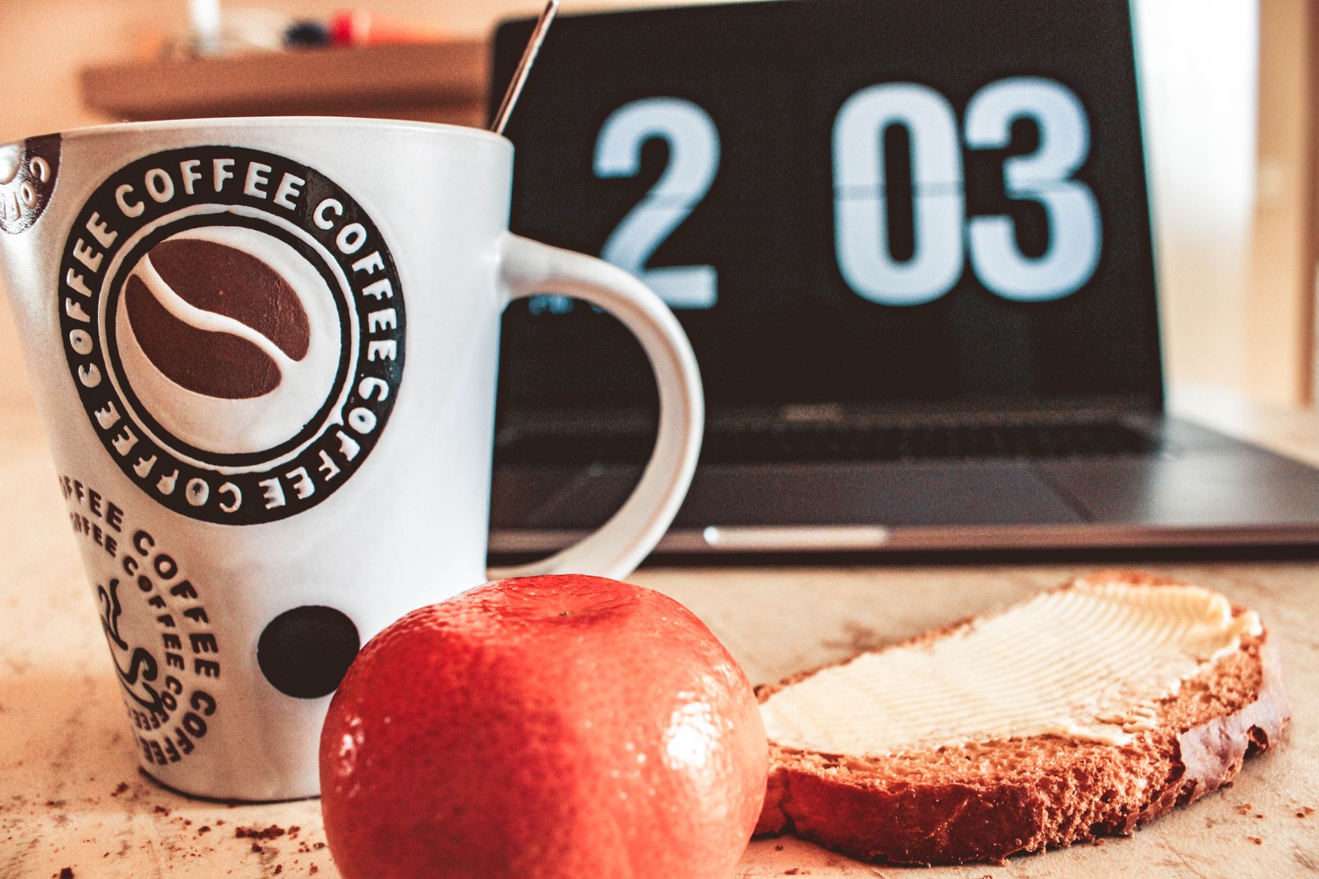 Hyggeligt morgenbord med kaffe, brød og frugt ved siden af en bærbar computer